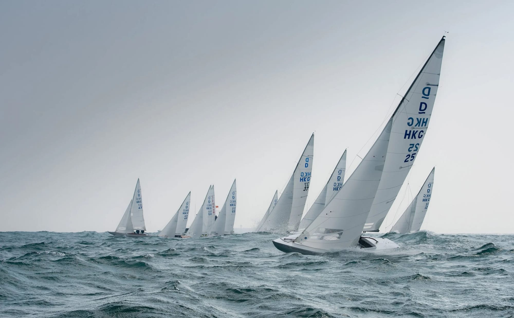 A fleet of Hong Kong Dragon keelboats racing upwind on a grey day off Hong Kong