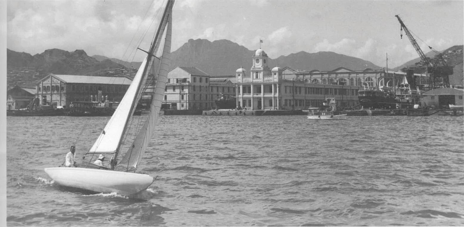Black and white harbour scene circa 1950 with a sailboat and waterfront clock tower.