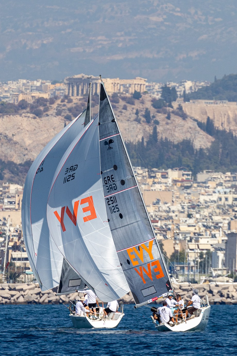 Two keelboats under spinnaker off Piraeus, the Acropolis on the hill behind them