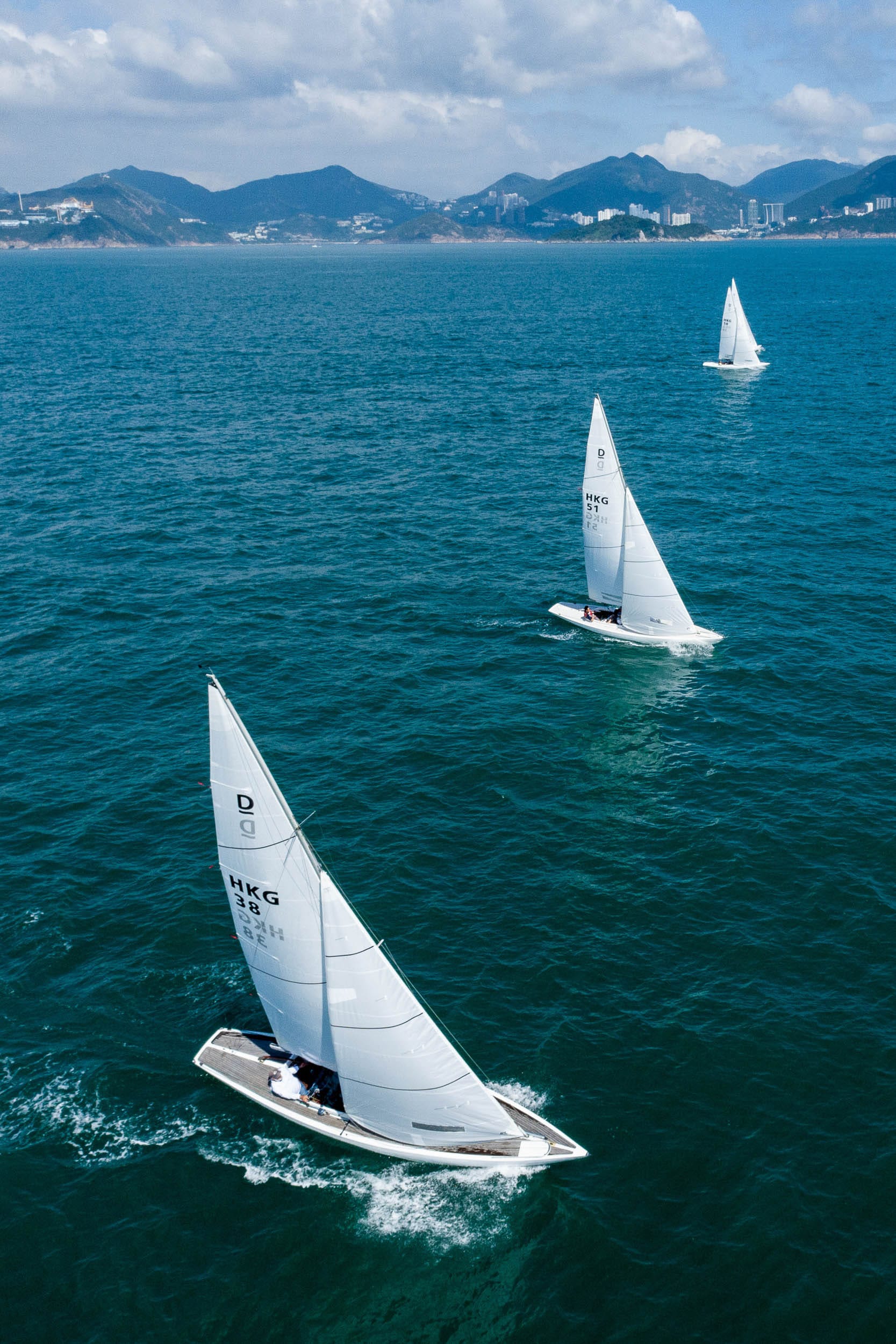Three Dragon keelboats racing in open water off Hong Kong, with green hills and the coastline behind.